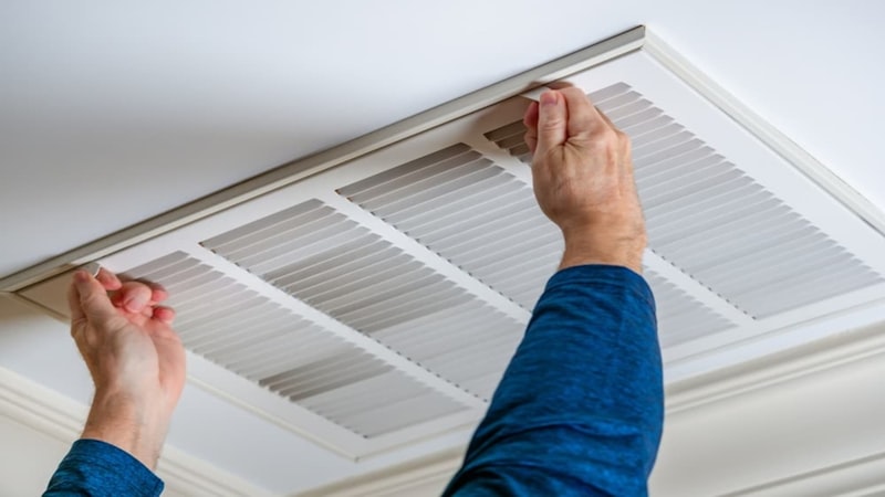 Technician opening a ceiling return vent to change the filter